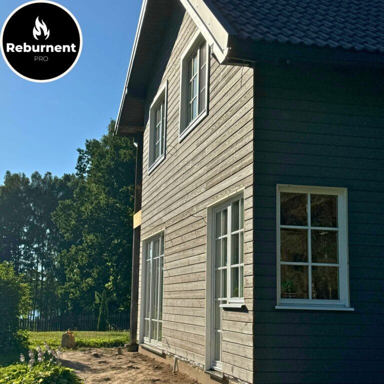 Dviejų aukštų namas su pilkai rudu degintos medienos fasadu ir baltais langų rėmais