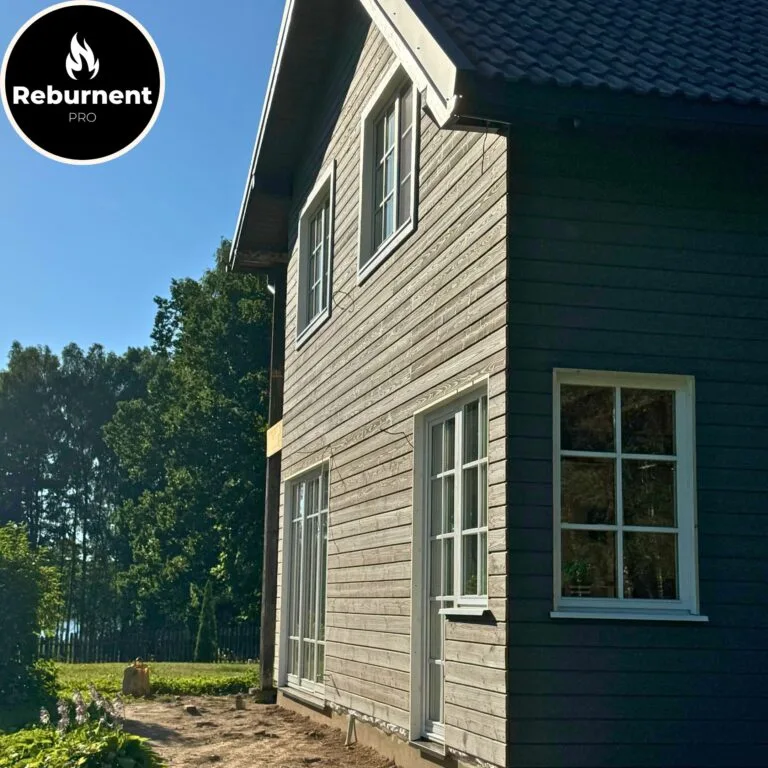 Dviejų aukštų namas su pilkai rudu degintos medienos fasadu ir baltais langų rėmais